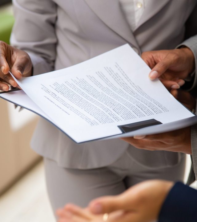 Diverse business partners reading contract together. Business man and woman wearing formal suits, standing and holding open folder with document. Agreement concept